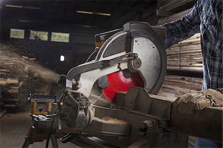 A reclaimed lumber workshop. A man in protective eye goggles using a circular saw to cut timber. Stock Photo - Premium Royalty-Free, Code: 6118-07353422