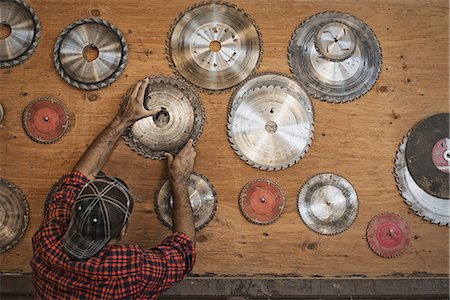 simsearch:6118-07353387,k - A reclaimed lumber workshop. A man reaching up to a storage board for circular saw blades to replace a blade. Foto de stock - Sin royalties Premium, Código: 6118-07353426