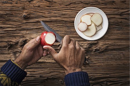 simsearch:6118-07353427,k - A person holding and slicing sections of a red skinned apple. Foto de stock - Sin royalties Premium, Código: 6118-07353437