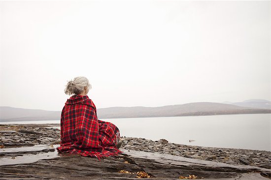 A woman looking out over the water on the shores of a calm lake, wrapped in a tartan rug. Photographie de stock - Premium Libres de Droits, Le code de l’image : 6118-07353560