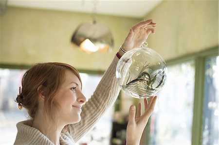 A woman holding up a large glass sphere, clear glass with a decorative objects inside. Stock Photo - Premium Royalty-Free, Code: 6118-07353590