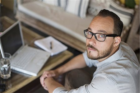 propriétaire - A man sitting at a desk using a laptop computer. Running a small business. Photographie de stock - Premium Libres de Droits, Code: 6118-07353594
