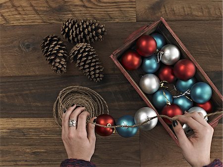 A woman threading Christmas shiny round ornaments on a piece of string. A small group of pine cones. Stock Photo - Premium Royalty-Free, Code: 6118-07353501