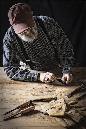 schreinerei - A man working in a reclaimed lumber yard workshop. Holding tools and sanding knotted and uneven piece of wood. Stockbilder - Premium RF Lizenzfrei, Bildnummer: 6118-07353644