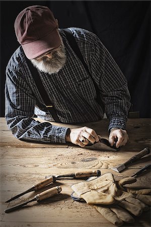 A man working in a reclaimed lumber yard workshop. Holding tools and sanding knotted and uneven piece of wood. Stock Photo - Premium Royalty-Free, Code: 6118-07353644