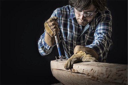 A man working in a reclaimed lumber yard workshop. Holding tools and extracting nails from a knotted and uneven piece of wood. Stock Photo - Premium Royalty-Free, Code: 6118-07353646