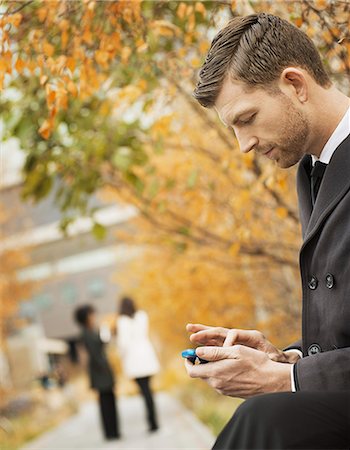 simsearch:6118-07354474,k - City life. A man in the park checking and texting, keeping in contact, using a mobile phone. Foto de stock - Sin royalties Premium, Código: 6118-07353687