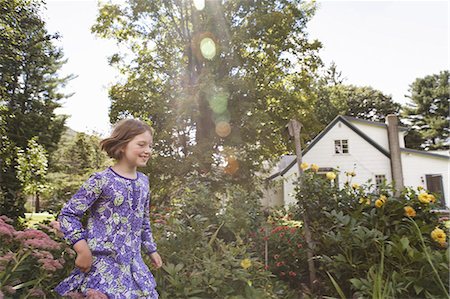 A child in a patterned blue dress running through a house garden. Photographie de stock - Premium Libres de Droits, Code: 6118-07353600