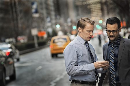 person on smart phone - Two men standing together looking at a cell phone display on a busy street at dusk. Photographie de stock - Premium Libres de Droits, Code: 6118-07353613