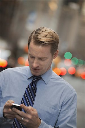 simsearch:6118-07353613,k - A man in a shirt and tie checking his cell phone, standing on a busy street. Photographie de stock - Premium Libres de Droits, Code: 6118-07353616