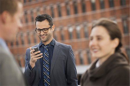 Three people, two in the foreground, and a man looking at a cell phone display. Photographie de stock - Premium Libres de Droits, Code: 6118-07353623