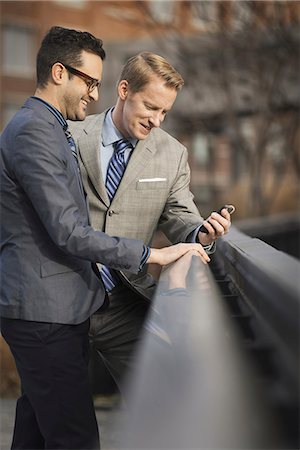 simsearch:6118-07353621,k - Two men in formal business clothes, standing side by side, looking at a cell phone screen or mobile phone. Fotografie stock - Premium Royalty-Free, Codice: 6118-07353620