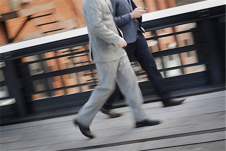 Two men in business clothes walking along a city sidewalk. Stock Photo - Premium Royalty-Free, Code: 6118-07353626