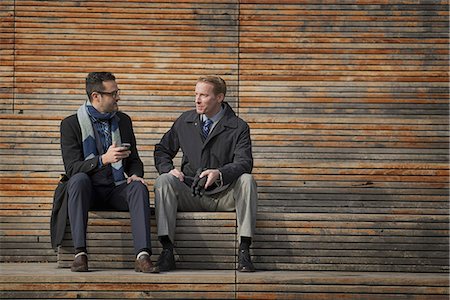 simsearch:6118-07353621,k - Two men sitting on a bench outside a large building in the city. One checking his mobile phone. Fotografie stock - Premium Royalty-Free, Codice: 6118-07353628