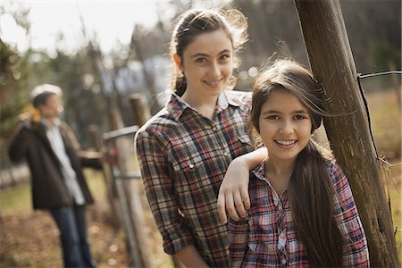 Two young girls beside a paddock fence, and a man in the background. An organic farm. Photographie de stock - Premium Libres de Droits, Code: 6118-07353764