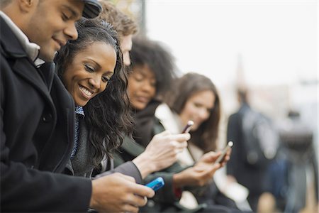 phone lines - City life. A group of people on the go, keeping in contact, using mobile phones. Men and women standing in a line. Looking up and laughing. Stock Photo - Premium Royalty-Free, Code: 6118-07353700