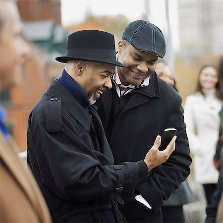 five people - City life. Two men standing side by side, keeping in contact, using mobile phones, and checking the screen, laughing.. Stock Photo - Premium Royalty-Free, Code: 6118-07353702