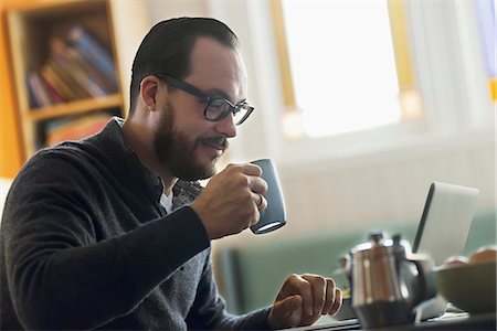 simsearch:6118-07440248,k - A bearded man having a drink of coffee. An open laptop computer on the counter. Photographie de stock - Premium Libres de Droits, Code: 6118-07353733