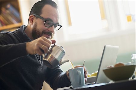 A bearded man having a drink of coffee. An open laptop computer on the counter. Stock Photo - Premium Royalty-Free, Code: 6118-07353732