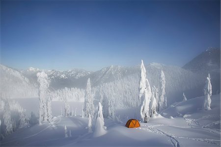 A bright orange tent among snow covered trees, on a snowy ridge overlooking a mountain in the distance. Fotografie stock - Premium Royalty-Free, Codice: 6118-07353842