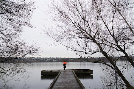 simsearch:6118-07351263,k - A woman standing at the end of a dock with an orange umbrella on a cloudy, grey day in Seattle. Foto de stock - Sin royalties Premium, Código: 6118-07353829