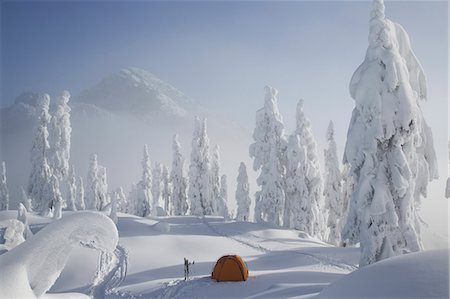 A bright orange tent sits on a snowy ridge overlooking a mountain in the distance. Foto de stock - Royalty Free Premium, Número: 6118-07353835