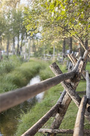 simsearch:6102-08760728,k - A rural scene, view over a fence made of wooden posts. A small stream. Trees with vivid green leaves. Stock Photo - Premium Royalty-Free, Code: 6118-07354088