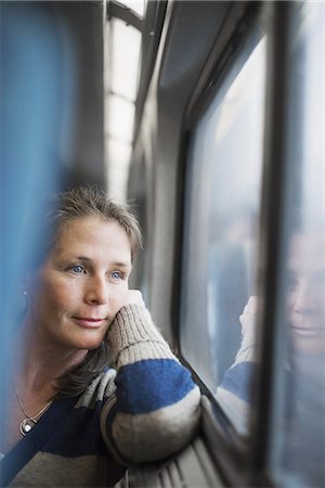 A woman sitting at a window seat in a train carriage, resting her head on her hand. Looking into the distance. Stock Photo - Premium Royalty-Free, Code: 6118-07354146