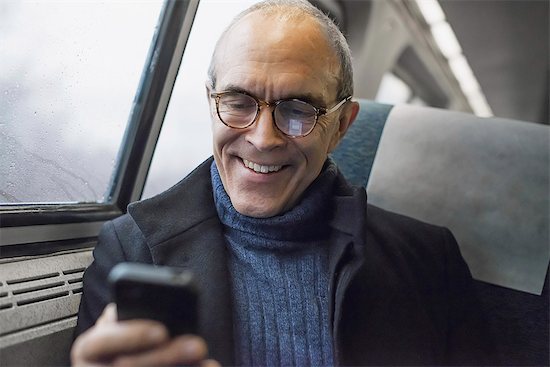A mature man sitting by a window in a train carriage, using his mobile phone, keeping in touch on the move. Stock Photo - Premium Royalty-Free, Image code: 6118-07354154
