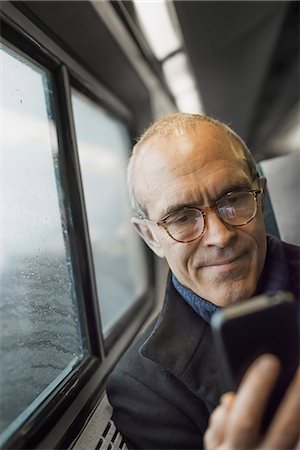 A mature man sitting by a window in a train carriage, using his mobile phone, keeping in touch on the move. Photographie de stock - Premium Libres de Droits, Code: 6118-07354155