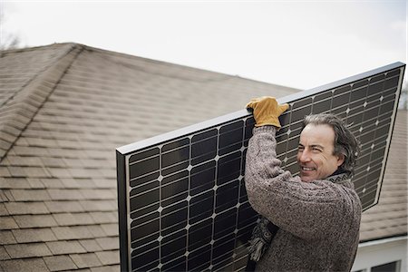 simsearch:6118-07354199,k - A man carrying a large solar panel across a farmyard. Foto de stock - Royalty Free Premium, Número: 6118-07354194