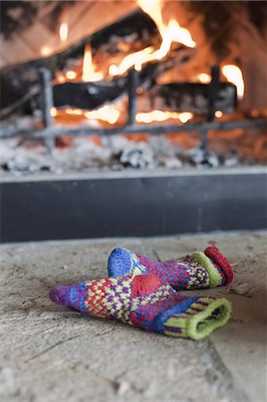 A log fire in a hearth with glowing heart, and flames. Patterned knitted woollen gloves. Stock Photo - Premium Royalty-Free, Code: 6118-07354123