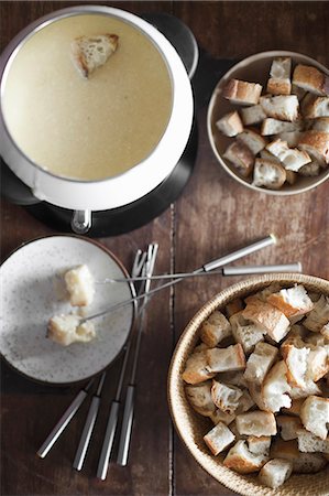 staple food - A cheese fondue on a table top. Cubed bread and long forks, for dipping bread into rich melted cheese mixture. Photographie de stock - Premium Libres de Droits, Code: 6118-07354122