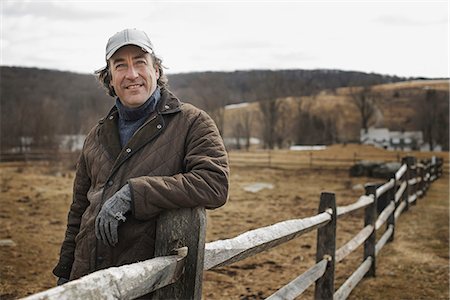 simsearch:6118-07354199,k - A man leaning against a post and rail fence on a farm in winter. Foto de stock - Royalty Free Premium, Número: 6118-07354202