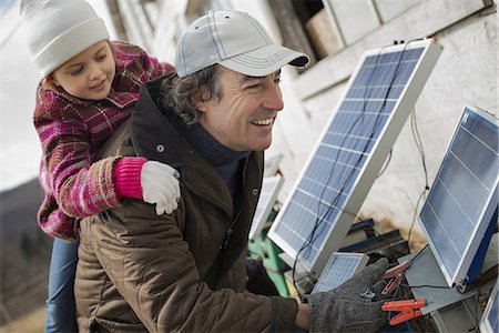 energy and power - A man giving a child a piggybank while trying to connect the leads for solar power panels. Stock Photo - Premium Royalty-Free, Code: 6118-07354205