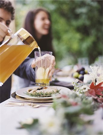 A group of people around a table in a garden. A celebration meal, with table settings and leafy decorations. A person pouring drinks into glasses. Photographie de stock - Premium Libres de Droits, Code: 6118-07354379