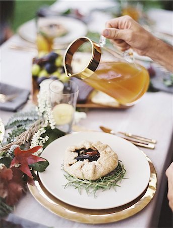 A group of people around a table in a garden. A celebration meal, with table settings and leafy decorations. A person pouring drinks into glasses. Photographie de stock - Premium Libres de Droits, Code: 6118-07354381