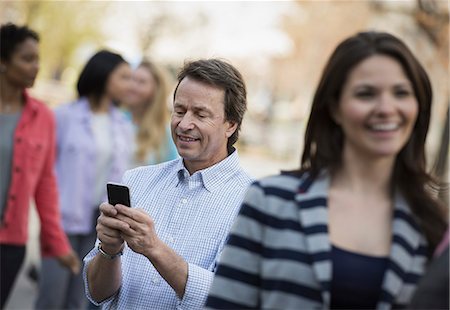 People outdoors in the city in spring time. A man checking his cell phone, among a group of men and women. Stock Photo - Premium Royalty-Free, Code: 6118-07354315