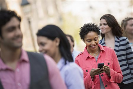 People outdoors in the city in spring time. A woman standing among a group checking her cell phone. Stock Photo - Premium Royalty-Free, Code: 6118-07354319