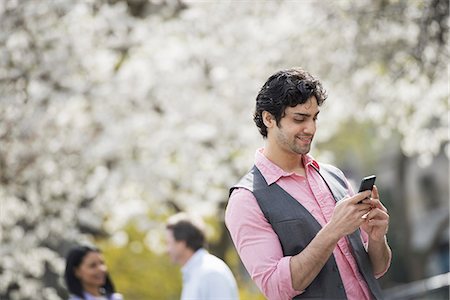 simsearch:695-03380830,k - People outdoors in the city in spring time. White blossom on the trees. A young man checking his cell phone. Foto de stock - Sin royalties Premium, Código: 6118-07354323