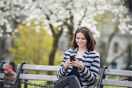 sitting on bench - Outdoors in the city in spring time. New York City park. White blossom on the trees. A woman sitting on a bench holding her mobile phone. Stock Photo - Premium Royalty-Free, Code: 6118-07354329