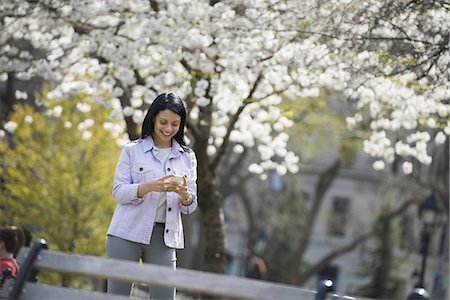 simsearch:6118-07354568,k - Outdoors in the city in spring time. New York City park. White blossom on the trees. A woman holding her mobile phone and smiling. Stock Photo - Premium Royalty-Free, Code: 6118-07354336