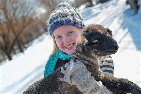 Winter scenery with snow on the ground. A young girl holding a young lamb. Stock Photo - Premium Royalty-Free, Code: 6118-07354457