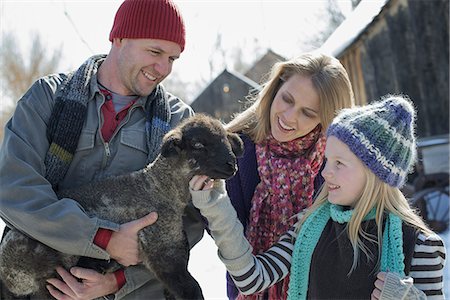 Winter scenery with snow on the ground. A man holding a young lamb, and a child stroking its chin. Photographie de stock - Premium Libres de Droits, Code: 6118-07354456