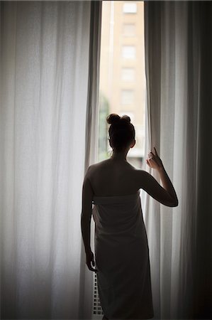 simsearch:6118-07354480,k - A young woman with her hair up, wearing a bath towel, looking through long curtains at a window. Stock Photo - Premium Royalty-Free, Code: 6118-07354475