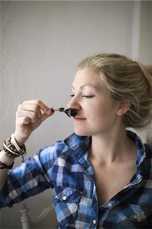 A young woman with blonde hair, holding a aromatic plant or herb flower to her nose and inhaling the aroma. Stock Photo - Premium Royalty-Free, Code: 6118-07354480