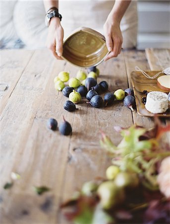 A woman at a domestic kitchen table. Arranging fresh fruit, black and green figs on a cheese board. Organic food. From farm to plate. Stock Photo - Premium Royalty-Free, Code: 6118-07354402