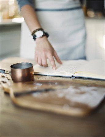 A woman in a domestic kitchen, reading a recipe book. Stock Photo - Premium Royalty-Free, Code: 6118-07354423