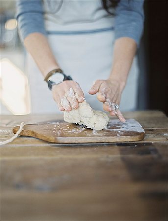 A domestic kitchen. A cook preparing pastry, mixing it by hand on a tabletop. Stock Photo - Premium Royalty-Free, Code: 6118-07354427