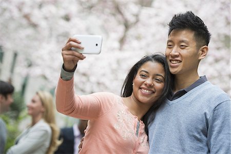 City life in spring. Young people outdoors in a city park. A couple taking a self portrait or selfy with a smart phone. Stock Photo - Premium Royalty-Free, Code: 6118-07354549